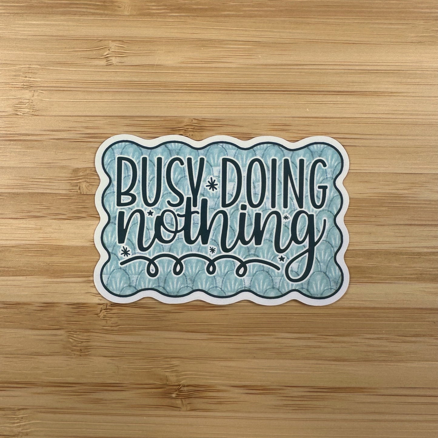 a sticker that says busy doing nothing on a wooden surface