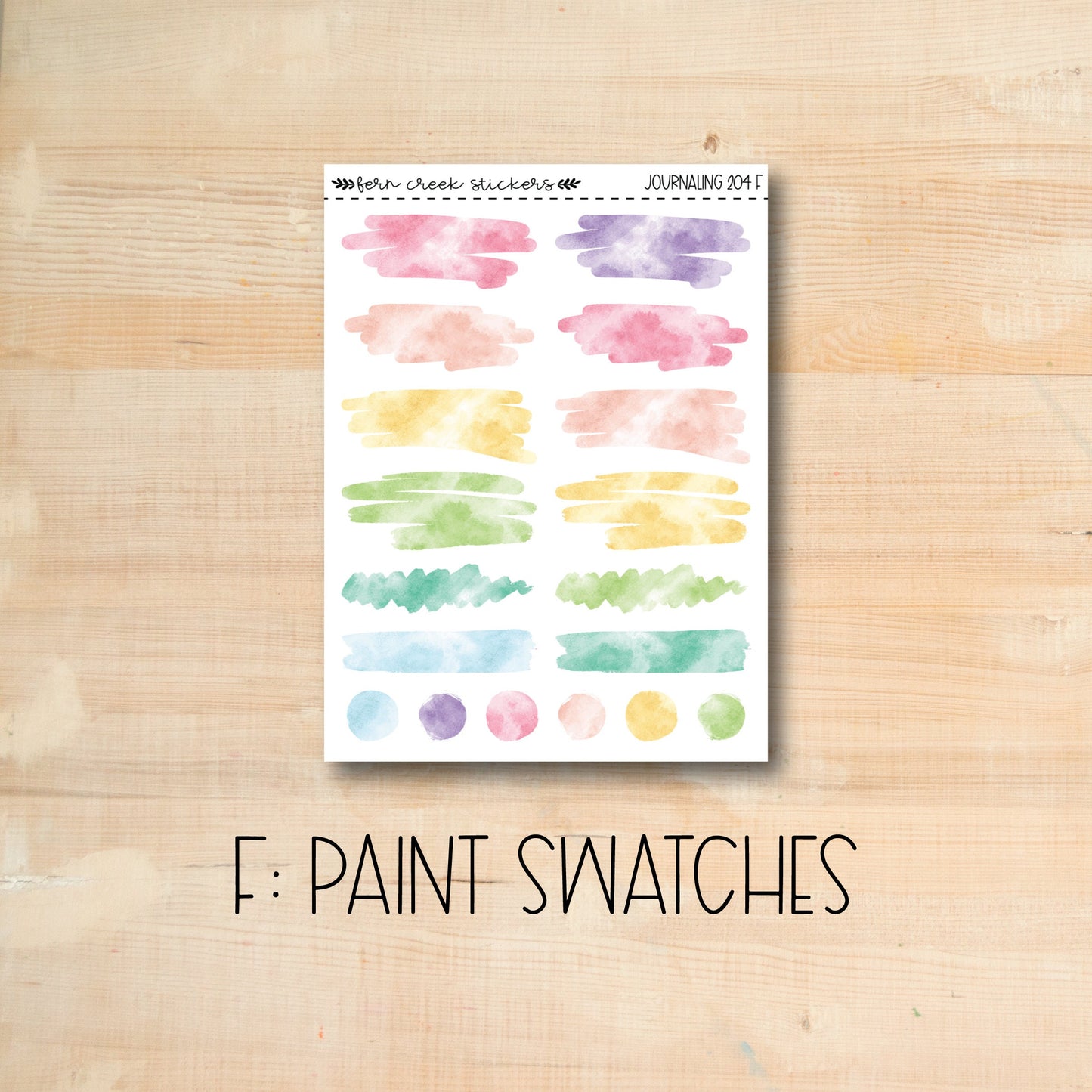 a wooden table topped with a sheet of paper covered in watercolor paint swatches